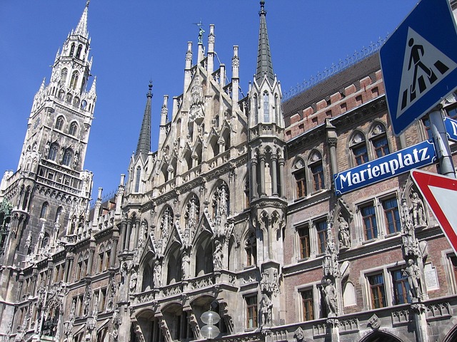 Beschreibung: Man sieht das Rathaus von München, mit einem strahlend blauen Himmel. Davor steht rechts die Straßenbeschilderung "Marienplatz"